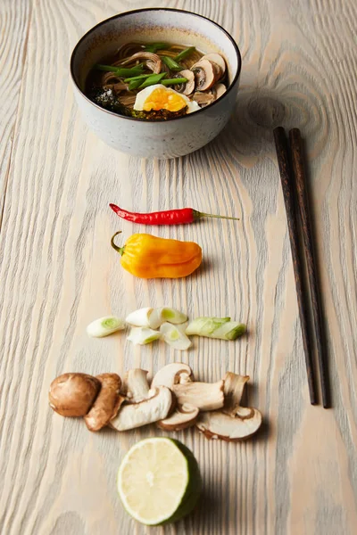 Ramen picante tradicional em tigela perto de pauzinhos e ingredientes em mesa de madeira — Fotografia de Stock