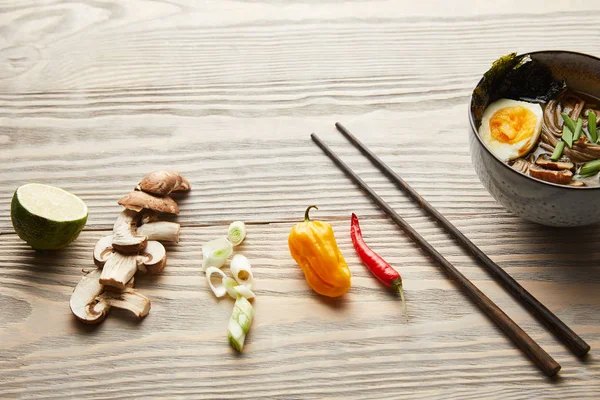 Ramen picante tradicional em tigela perto de pauzinhos e ingredientes em mesa de madeira — Fotografia de Stock