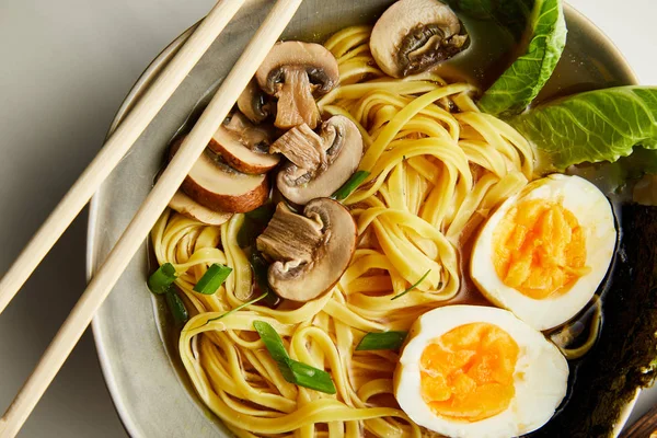 Close up view of traditional asian ramen in bowl with chopsticks on grey surface — Stock Photo
