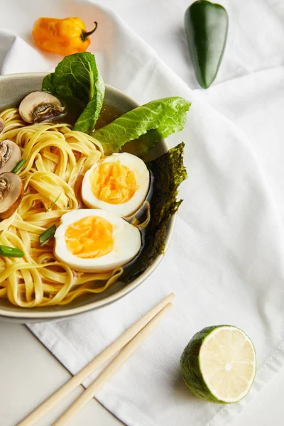 Tradicional asiático ramen em tigela perto de pauzinhos, guardanapo e ingredientes na superfície cinza — Fotografia de Stock