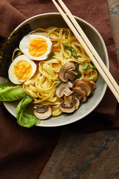 Top view of traditional spicy ramen in bowl with chopsticks on brown napkin on stone surface — Stock Photo