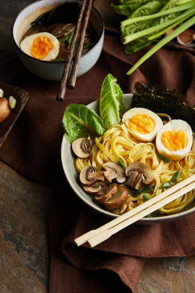 Traditional spicy ramen in bowls with chopsticks on brown napkin on stone surface — Stock Photo