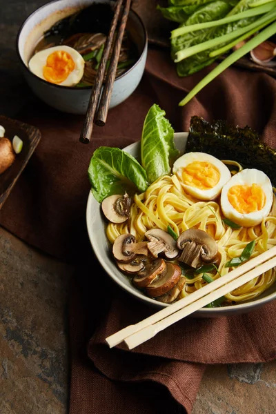 Traditionelle würzige Ramen in Schalen mit Essstäbchen auf brauner Serviette auf Steinoberfläche — Stockfoto