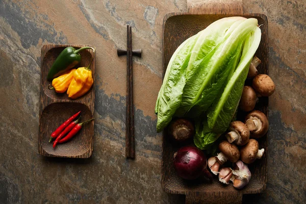 Вид сверху на палочки для еды и свежие овощи на каменной поверхности — стоковое фото