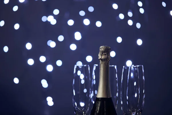 Bottle of sparkling wine and glasses with blurred christmas lights — Stock Photo
