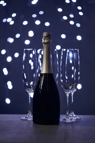Bottle of sparkling wine and glasses with blue christmas lights bokeh — Stock Photo