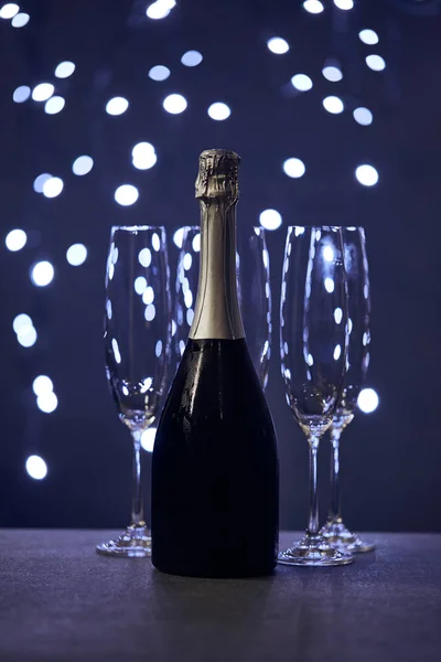 Bouteille de vin mousseux et des verres avec des lumières de Noël bleu bokeh — Photo de stock