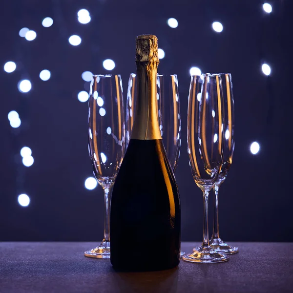 Botella de champán y copas con luces navideñas bokeh - foto de stock