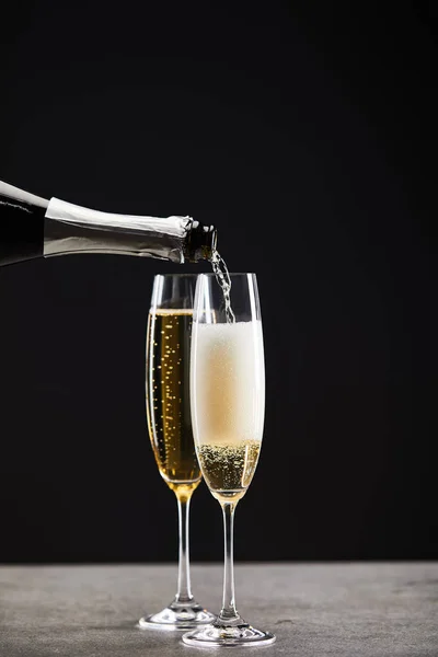 Sparkling wine pouring from bottle into glasses for celebrating christmas on black — Stock Photo