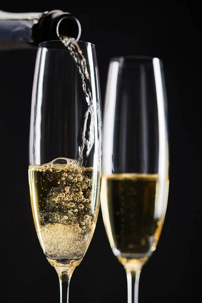 Gros plan de champagne versé de la bouteille dans des verres pour célébrer Noël, isolé sur noir — Photo de stock