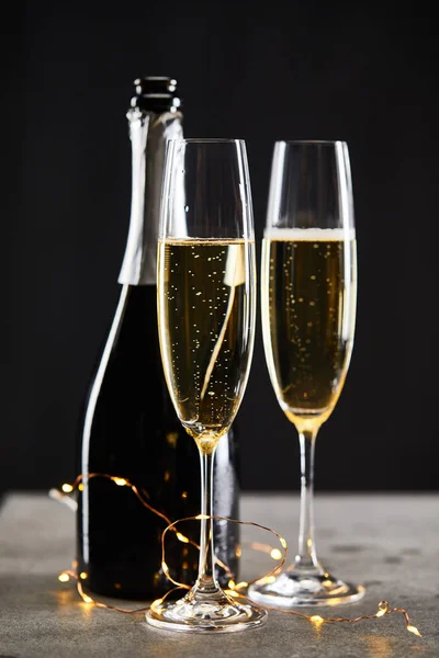 Sparkling wine in glasses and bottle with yellow christmas lights, on black — Stock Photo