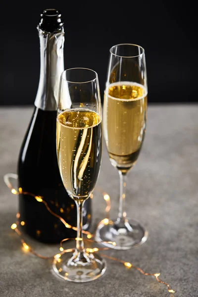 Verres et bouteille avec champagne et lumières de Noël jaunes, sur noir — Photo de stock