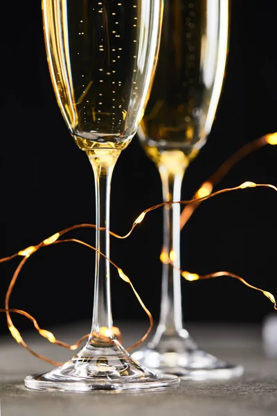 Primer plano de vino espumoso tradicional en vasos con luces de Navidad amarillas, en negro - foto de stock
