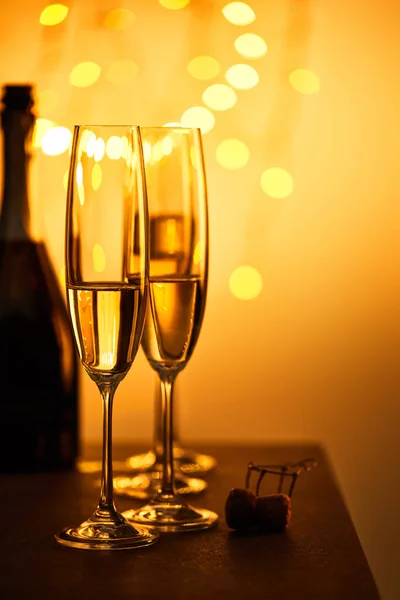 Corcho, botella y vasos con vino espumoso, con luces amarillas de navidad bokeh - foto de stock