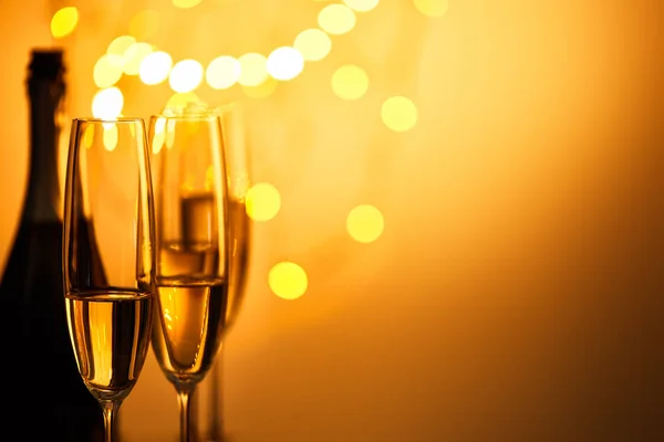 Copas y botella de vino espumoso con luces amarillas de Navidad bokeh — Stock Photo
