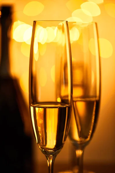 Glasses of champagne with blurred bottle and yellow christmas lights — Stock Photo