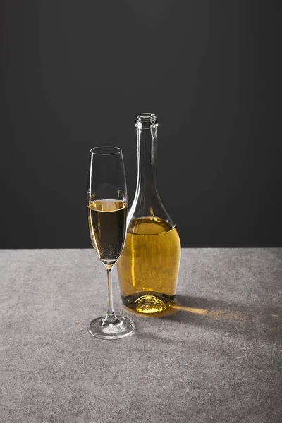 Glass and bottle of sparkling wine on grey — Stock Photo