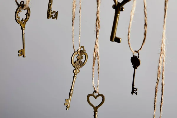 Vista de cerca de las llaves vintage colgando de cuerdas aisladas en gris - foto de stock