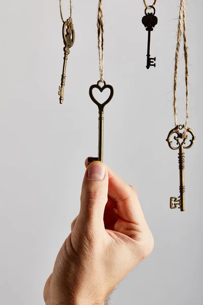 Vista ritagliata di uomo toccare chiavi vintage appeso su corde isolate su bianco — Foto stock