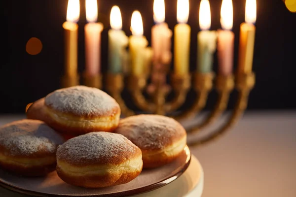 Foco seletivo de deliciosos donuts em stand perto de velas brilhantes em menorah no fundo preto com luzes bokeh em Hanukkah — Fotografia de Stock