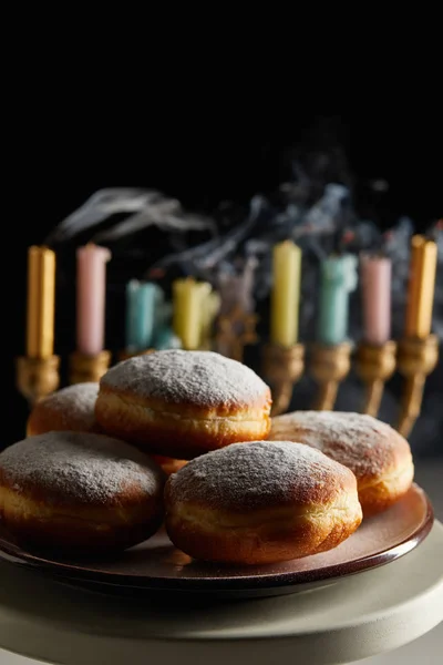 Selective focus of delicious doughnuts on stand near candles in menorah isolated on black — Stock Photo