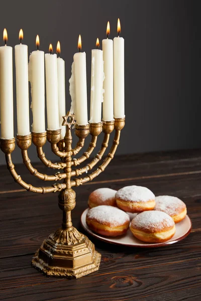 Deliciosos donuts perto de velas em chamas em menorah na mesa de madeira em Hanukkah isolado em cinza — Fotografia de Stock