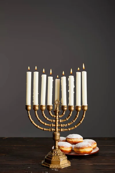 Deliciosos donuts perto de velas em chamas em menorah na mesa de madeira em Hanukkah isolado em cinza — Fotografia de Stock