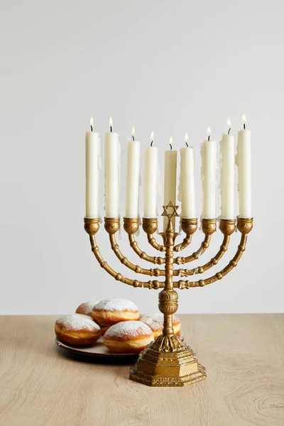 Deliciosos donuts perto de velas em chamas em menorah em Hanukkah isolado no branco — Fotografia de Stock