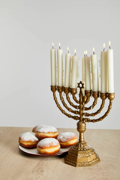 Delicious doughnuts near burning candles in menorah on Hanukkah isolated on white — Stock Photo