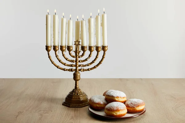 Deliciosos donuts perto de velas em chamas em menorah em Hanukkah isolado no branco — Fotografia de Stock