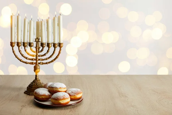 Deliciosos donuts perto de velas em menorah no fundo branco com luzes bokeh em Hanukkah — Fotografia de Stock