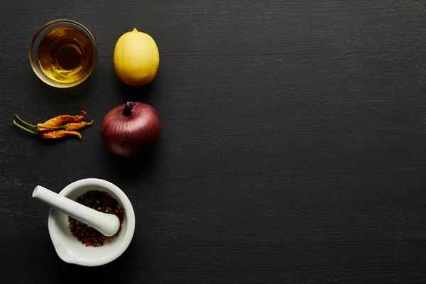 Top view of olive oil, chill peppers with lemon and onion on black wooden background — Stock Photo