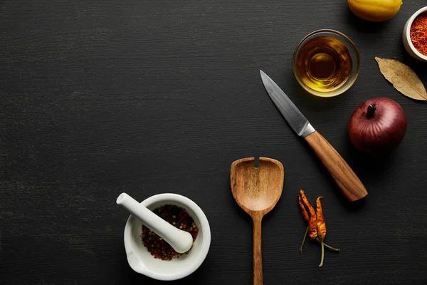 Top view of wooden spatula, knife with spices and olive oil on black wooden background — Stock Photo