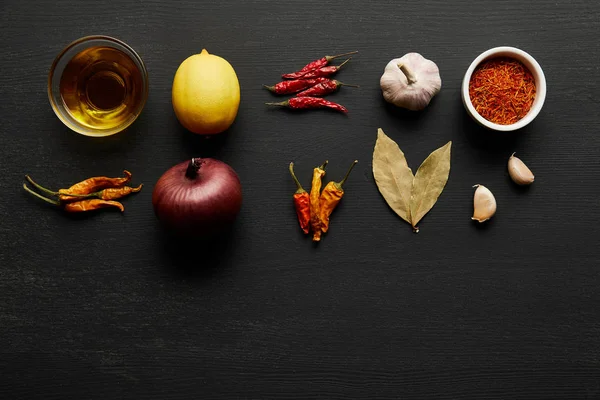 Top view of spices, olive oil with onion and lemon on black wooden background — Stock Photo