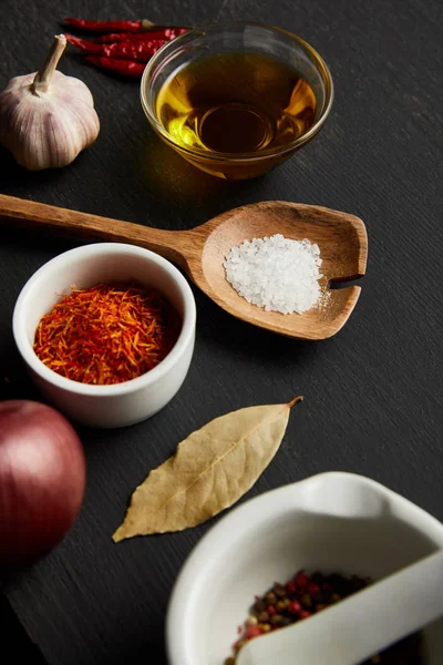 Spices, chili peppers with salt on wooden spoon and olive oil on black wooden background — Stock Photo