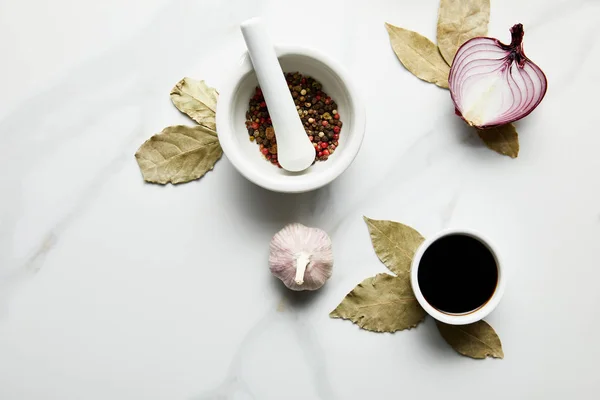 Vista dall'alto di grani di pepe, salsa di soia con cipolla e aglio su foglie di alloro su sfondo di marmo — Foto stock