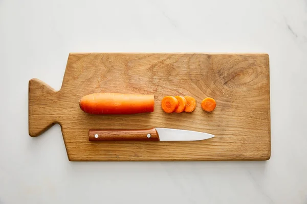 Top view of carrot with slices and knife on cutting board on marble background — Stock Photo