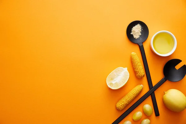 Vista superior de los utensilios de cocina con aceite de oliva, verduras y limones sobre fondo naranja - foto de stock
