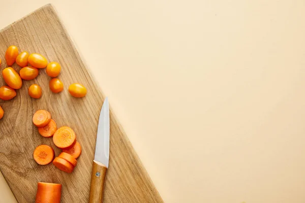 Vista superior de tomates de zanahoria y cereza con cuchillo en tabla de cortar sobre fondo beige - foto de stock