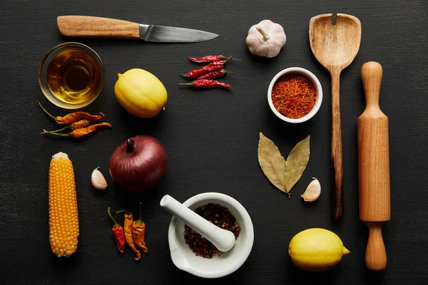 Vista superior de utensílios de cozinha de madeira com legumes maduros e especiarias em fundo de madeira preta — Fotografia de Stock