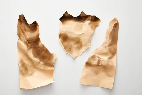Vista superior de pedazos de papel vintage beige arrugado y quemado sobre fondo blanco - foto de stock