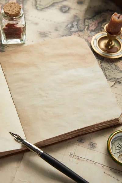 Винтажный чистый блокнот с перьевой ручкой возле компаса и свечи на фоне карты — стоковое фото