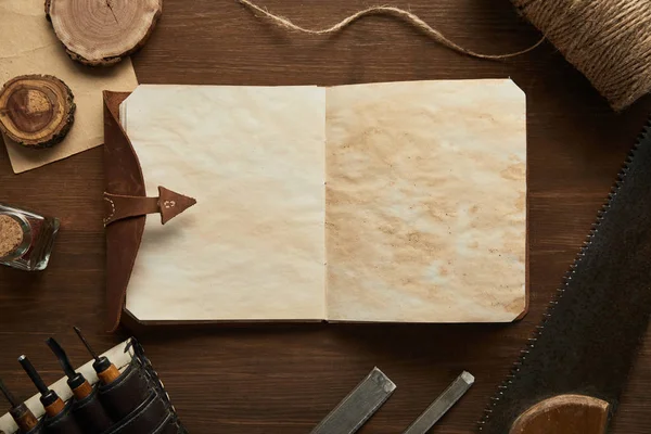 Vue du dessus des outils de menuiserie vieillis près d'un carnet vintage vierge sur une table en bois — Photo de stock