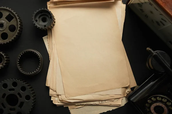 Vista superior de engranajes envejecidos y papel en blanco vintage cerca del reloj vintage en la superficie negra - foto de stock