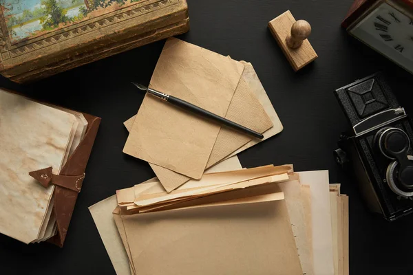 Top view of vintage camera, paper, painting, fountain pen, clock, stamp and notepad on black background — Stock Photo