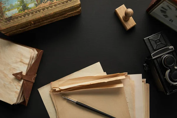 Vue du dessus de l'appareil photo vintage, papier, peinture, stylo plume, horloge, timbre et bloc-notes sur fond noir — Photo de stock