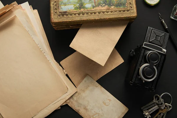 Top view of vintage camera, paper, painting, fountain pen, keys on black background — Stock Photo