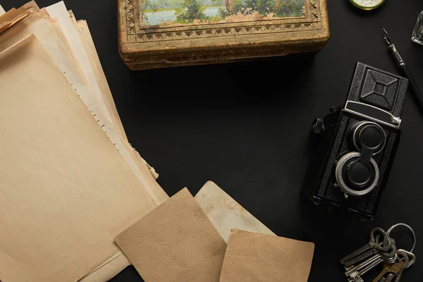 Vista superior da câmera vintage, papel, pintura, caneta-tinteiro, chaves no fundo preto — Fotografia de Stock