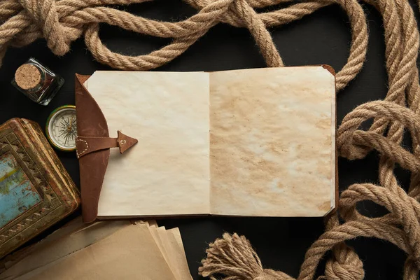 Top view of vintage notebook, rope, compass and painting on black background — Stock Photo