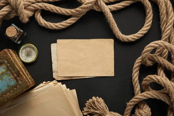 Vue de dessus du papier vintage, corde, boussole et peinture sur fond noir — Photo de stock